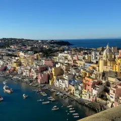 Vue panoramique de Procida ou Ischia, avec ses maisons colorées nichées sur la côte et des bateaux dans le port.
