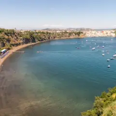 Vue d'une baie pittoresque, avec une plage de sable noir, des falaises verdoyantes et une multitude de bateaux dans l'eau bleue. Un paysage qui rappelle la voisine de Capri.
