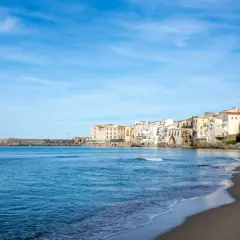 Vue de la plage et des maisons colorées de Cefalù, Sicile, sous un ciel bleu clair.