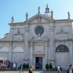 Façade de Santa Maria Formosa à Venise, avec des statues, un dôme et une place animée.