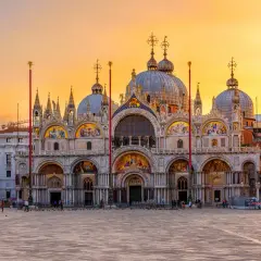 Magnifique coucher de soleil sur la place Saint-Marc, idéal pour visiter la basilique Saint-Marc. La façade ornée de mosaïques brille sous le ciel orangé.