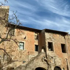 Bâtiments anciens et décrépits, avec une tour de briques penchée, sous un ciel bleu et nuageux. Une promenade sur la Via Appia à pied révèle ces ruines.