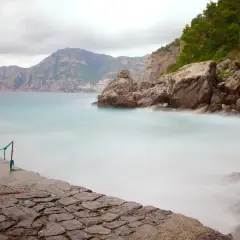 Vue brumeuse de la côte rocheuse de Praiano, Italie, avec des vagues douces et des montagnes en arrière-plan.