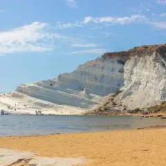 La Scala dei Turchi, une falaise blanche spectaculaire en Sicile, se dresse au-dessus d'une plage de sable doré et d'une mer bleue. Des visiteurs explorent ses terrasses naturelles.