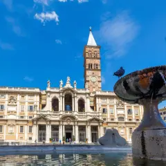 La basilique Sainte-Marie-Majeure se dresse fièrement sous un ciel bleu, avec une fontaine et des pigeons au premier plan.