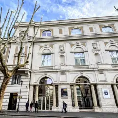 Le **Palazzo Merulana**, un édifice élégant, se dresse sous un ciel bleu nuageux, orné d'arbres dénudés aux branches graphiques.