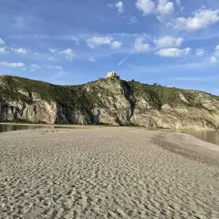 Plage de Patti, Sicile. Un château domine la colline rocheuse surplombant la mer calme et la plage de sable.
