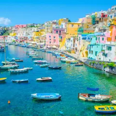 Un charmant port sur une île près de Naples, avec des maisons colorées et de nombreux bateaux dans l'eau turquoise.