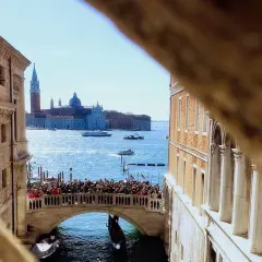 Vue d'un pont vénitien animé, avec des gondoles et des bateaux sur le canal, et des bâtiments historiques en arrière-plan.