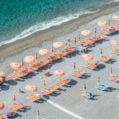 Lignes d'orange vif et de parasols colorés sur une plage de galets, une invitation à la détente. Destination Italie plage.