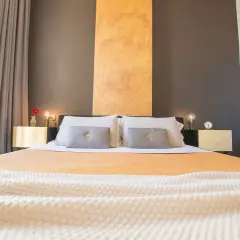 Lit et tables de chevet dorés dans une chambre d'hôte Italie du Nord. Rideaux gris et blancs, mur anthracite et ocre.