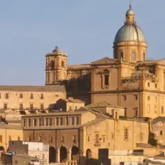 Vue panoramique de la ville de Piazza Armerina en Sicile, dominée par une imposante cathédrale à dôme vert.