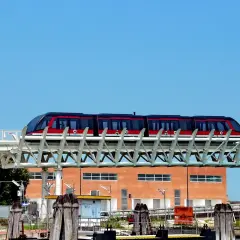 Le people mover de Venise, un train rouge et noir, circule sur une voie aérienne devant un bâtiment orange.