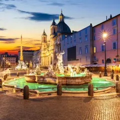 Fontaine de la piazza Navona illuminée au crépuscule, avec l'obélisque et l'église en arrière-plan.
