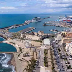 Vue aérienne du port de Civitavecchia, avec un immense paquebot de croisière, des bateaux, une forteresse historique et une grande roue.