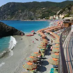 Plage animée à Moneglia, Italie, avec des parasols rayés, des baigneurs dans la mer turquoise et des collines verdoyantes en arrière-plan.