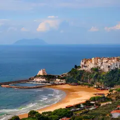 Vue d'un village pittoresque perché sur une falaise surplombant la mer, avec une plage de sable et un port. On dirait un **ostie** de **Rome** !