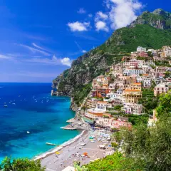 Vue spectaculaire de Positano, une ville pittoresque perchée sur une falaise en **Agerola, Italie**. Les maisons colorées descendent vers une plage animée et la mer d'un bleu profond.