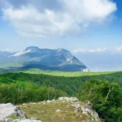 Vue panoramique des montagnes verdoyantes du Cilento, Italie, sous un ciel bleu parsemé de nuages blancs.