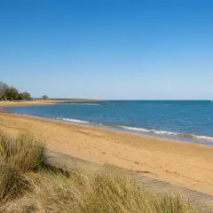 Plage de sable doré à Caorle, avec des parasols de chaume, des chaises blanches et la mer bleue sous un ciel clair.