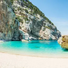 Plage de sable blanc bordée par des falaises imposantes et une eau turquoise cristalline. Un aperçu de ce à quoi ressemble la Riviera italienne.