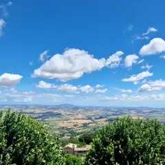 Vue panoramique depuis Cingoli, avec des champs ondulants et un ciel bleu parsemé de nuages blancs.