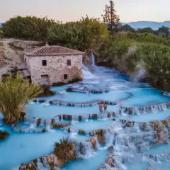Casciana Terme : un couple se promène dans les cascades d'eau thermale bleue, près d'une vieille bâtisse en pierre.