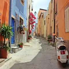 Ruelle colorée en Italie, parfaite pour une location de villa. Un scooter blanc attend, prêt pour l'aventure.
