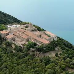 Vue aérienne de Populonia, Italie, un village médiéval perché sur une colline verdoyante surplombant la mer d'un bleu profond.
