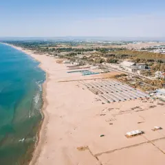 Vue aérienne d'une longue plage de sable fin bordée par la mer bleue, avec des rangées de parasols et des bâtiments à Catane, Sicile.
