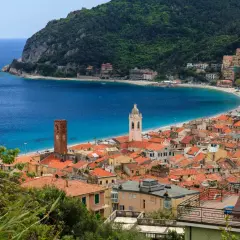 Vue d'un village pittoresque sur la côte de l'Italian Riviera, avec des maisons aux toits rouges, une plage de sable et une mer bleue étincelante.