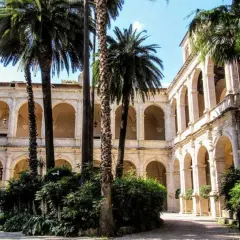 Cour intérieure avec palmiers, arcades et balcons, évoquant le Vittoriano et le Palazzo Venezia.
