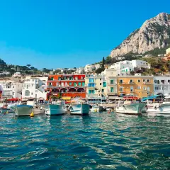 Vue du port de Capri, avec des bateaux blancs amarrés et des maisons colorées à flanc de colline. Un paysage typique de Capri, pas Ischia.