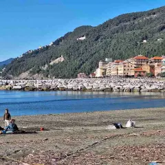 Vue de la plage de Chiavari avec des familles profitant du soleil, des bâtiments colorés et une colline verdoyante en arrière-plan.
