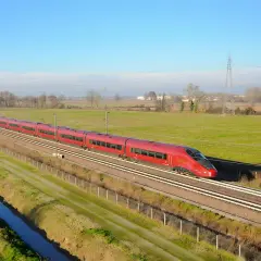 Le train rouge Italo file sur les voies, reliant Roma à Naples à travers la campagne verdoyante sous un ciel bleu.