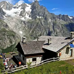 Refuge de montagne en pierre, idéal pour une location vacances Aoste Italie, avec des randonneurs profitant du paysage alpin spectaculaire.