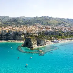 Vue aérienne de Tropea, avec ses maisons colorées perchées sur la falaise, une plage bondée et la mer d'un bleu turquoise éclatant.