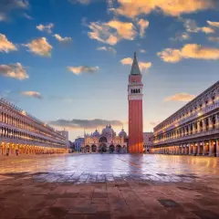 Le **place Saint-Marc à Venise** s'illumine au crépuscule. La basilique et le campanile se dressent majestueusement sous un ciel nuageux.