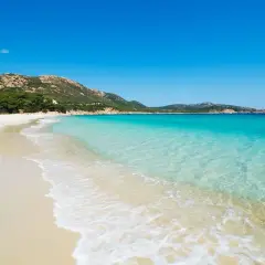 Plage de sable blanc bordée par une eau turquoise cristalline, avec des collines verdoyantes en arrière-plan. Un paysage idyllique d'**Italie bord de mer**.