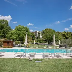 Piscine d'agritourisme au Lac de Garde, entourée de verdure, avec chaises longues et parasols sous un ciel bleu.