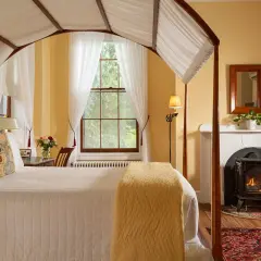 Chambre d'hôte en Italie : lit à baldaquin, cheminée, rocking-chair et vue sur la nature.
