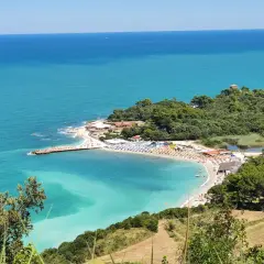 Vue panoramique de la baie de Portonovo, avec ses eaux turquoise, sa plage animée et sa végétation luxuriante.