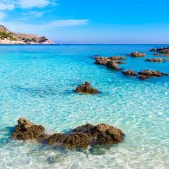 Eau turquoise cristalline, rochers émergeant de la mer, colline verdoyante en arrière-plan. Un rêve de toscane plage.