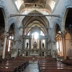 Intérieur de l'église Santo Stefano à Venise, avec ses bancs en bois, ses voûtes ornées et son autel baigné de lumière.