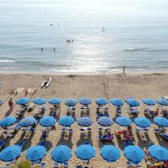 Plage de San Vincenzo en Toscane, avec des rangées de parasols bleus, des kayaks et des gens profitant de la mer.