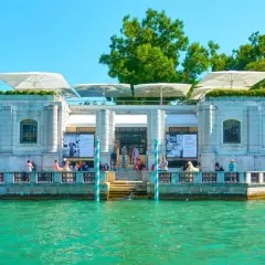 Le **Guggenheim Venise** se reflète dans l'eau turquoise. Des parasols blancs ombragent la terrasse où des visiteurs admirent l'architecture.