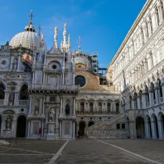 Le **Palais des Doges** à Venise, avec ses dômes, statues et arcades, se dresse majestueusement sous un ciel bleu.