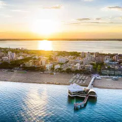 Coucher de soleil sur Lignano, Italie. La plage et la mer s'étendent à perte de vue, avec un pont moderne se jetant dans l'eau.