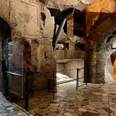 Intérieur des catacombes San Callisto. Un sarcophage blanc repose sous un arc de briques, dans un dédale de couloirs aux fresques anciennes.