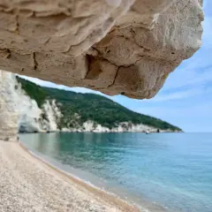 Vue depuis une grotte sur une plage de galets, mer turquoise et falaises blanches sur la côte adriatique Italie.